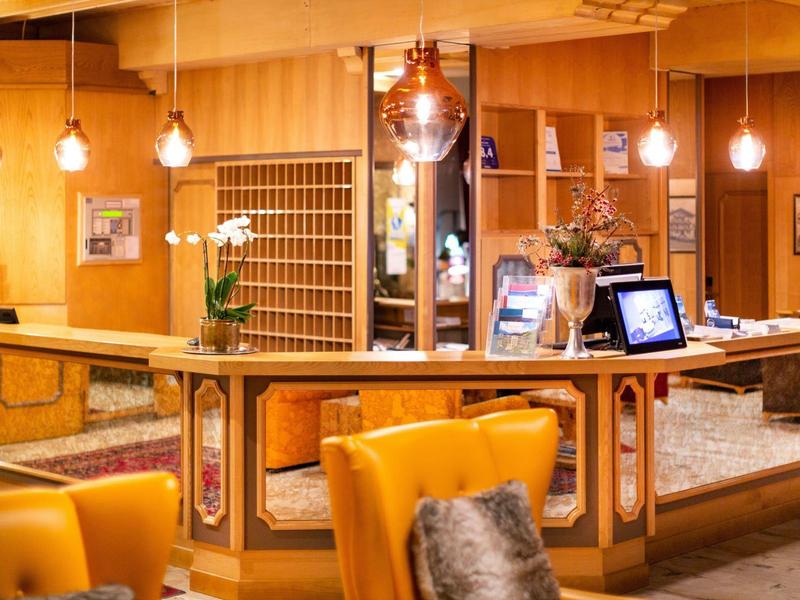 Innenraum eines Hotels mit gelben Sesseln, hölzernem Empfangstresen und warmen Pendelleuchten.
