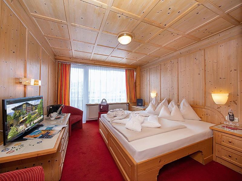 Gemütliches Holz-Zimmer mit Doppelbett, TV, roten Vorhängen und Teppichboden.