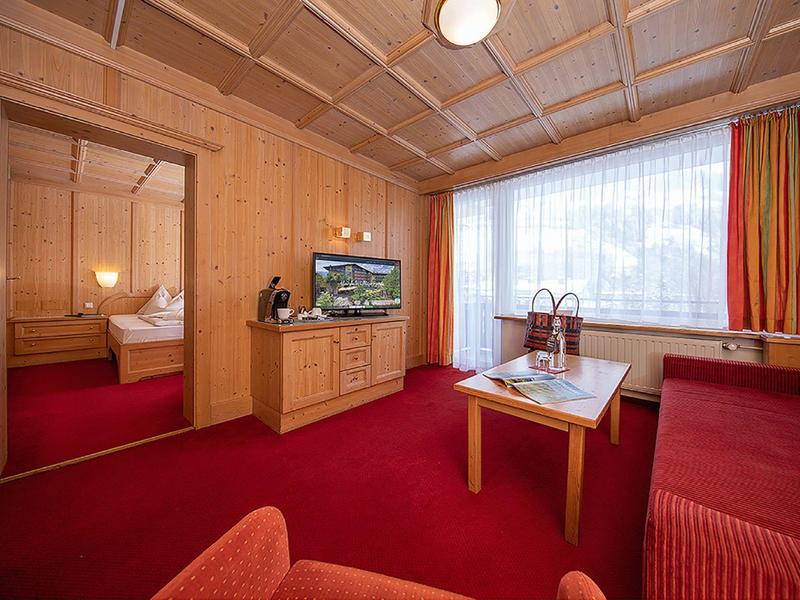 Gemütliches Wohnzimmer mit Holzwänden, rotem Teppich, Sofa, Fernseher und großem Fenster mit Vorhängen.