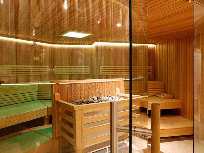 Helle Holzsauna mit Sitzbänken, Ofen und Glaswand, warmes, einladendes Licht.