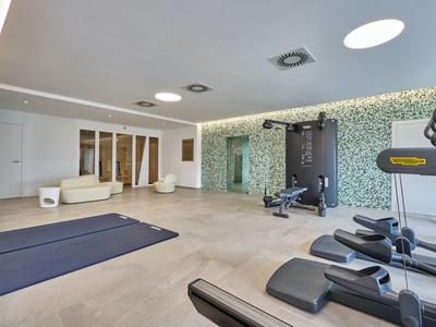 Moderní fitness místnost s běžeckými pásy, jógovými podložkami, činkami a posezením.