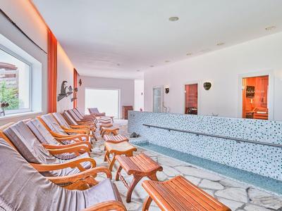 Heller Ruheraum mit Holzloungestühlen und blauer Polsterbank vor großen Fenstern und weißer Wand.