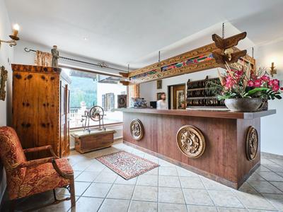 Světlá hotelová recepce s dřevěnou přepážkou, židlí, skříní a květinovou výzdobou.