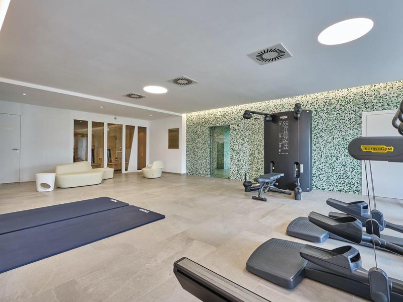 Moderner Fitnessraum mit Laufbändern, Hanteln, Yoga-Matten und hellen, glatten Bodenfliesen.