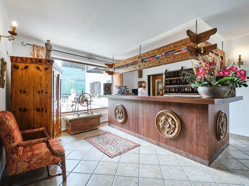 Heller Empfangsraum mit Holztheke, Sitzbank, Teppichen und Blumenarrangement am Tresen.