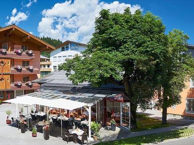 Meerdere gebouwen met buitenspeelruimtes omgeven door bomen en bergen op de achtergrond.