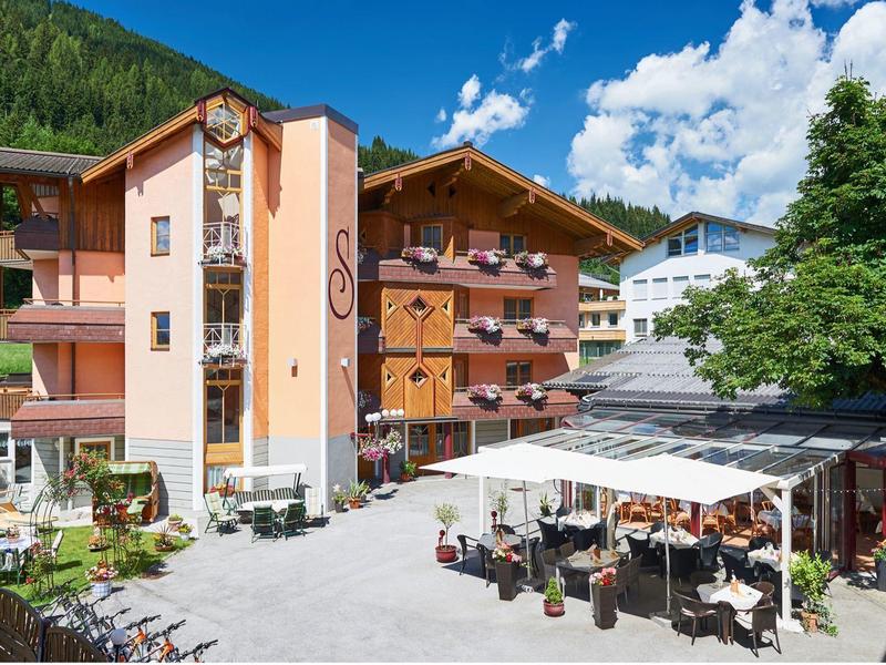 Mehrstöckiges Hotelgebäude mit Balkonen, Terrassenbereich und grüner Berglandschaft im Hintergrund.