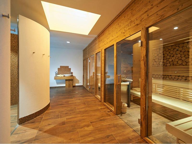 Moderner Wellnessraum mit Sauna, Holzverkleidung, großen Glastüren und gemütlicher Beleuchtung.