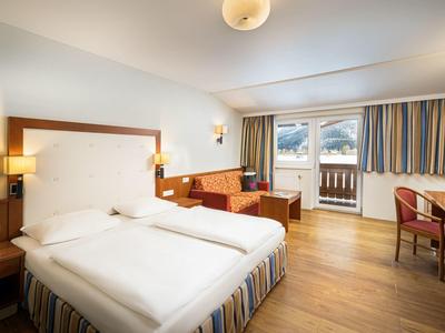 Helles Hotelzimmer mit Doppelbett, Holzmöbeln, Sofa, großem Fenster und Holzboden.
