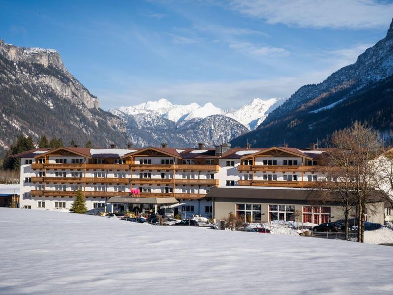 Großes Hotelgebäude vor verschneiten Bergen und blauem Himmel im Tal mit weißer Schneedecke.