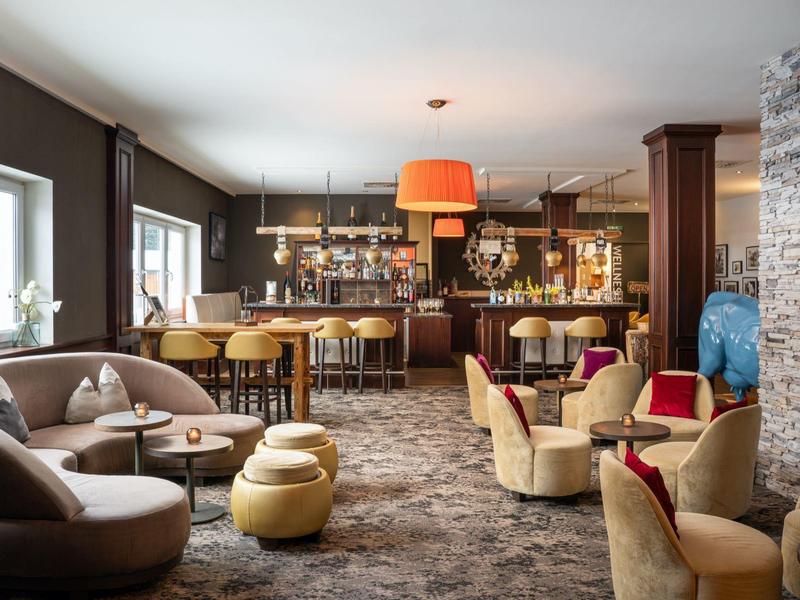 Elegante Hotelbar mit modernen Sesseln, Theke, runden Tischen und warmem, gemütlichem Licht.