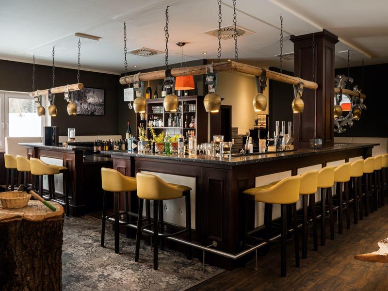 Moderne Bar mit gelben Barhockern, dunklem Holz und hängender Beleuchtung in warmem Ambiente.