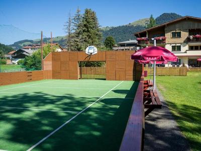 Boisko sportowe z koszem do koszykówki i bramką piłkarską, taras z parasolem i krzesłami, alpejski krajobraz