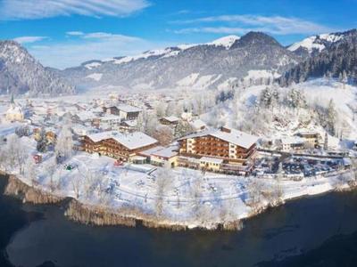 Zimowy krajobraz z zaśnieżoną wioską i górami nad jeziorem pod niebieskim niebem.