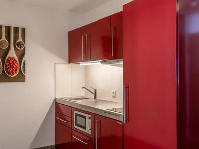 Kompaktní kuchyňka s červenými skříňkami, mikrovlnkou, dřezem a moderní stěnovou dekorací.