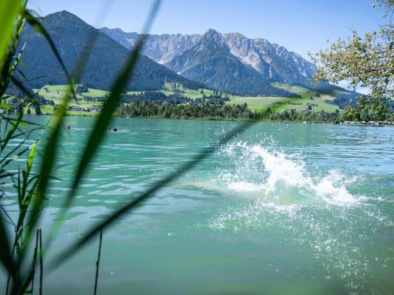 Stříkající voda po hodu kamenem do čistého horského jezera s Alpami v pozadí.