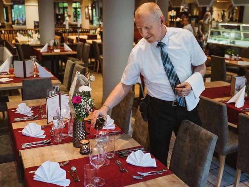 Číšník připravuje stůl v restauraci s červeno-bílým stolováním.