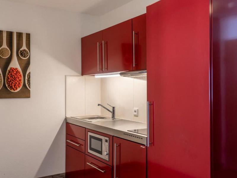 Kompaktní kuchyňka s červenými skříňkami, mikrovlnkou, dřezem a moderní stěnovou dekorací.