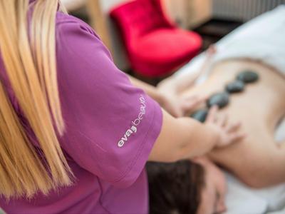 Therapeutin legt heiße Steine auf den Rücken einer Person zur Massage in hellem Raum.