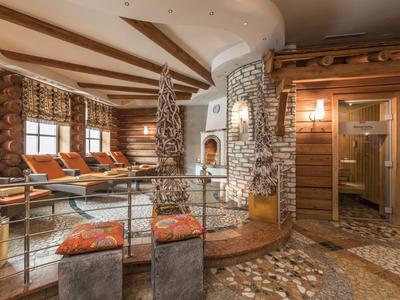 Rustikaler Wohnraum mit Steinmauer, Kamin, Holzbalken, bequemen Sesseln und warmen Erdtönen.