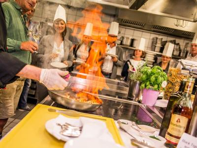 Chef prepares flambé dish in a restaurant kitchen surrounded by guests.