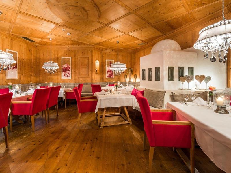 Gemütlicher Restaurantraum mit Holzwänden, roten Sesseln und weißen gedeckten Tischen unter Kronleuchtern.