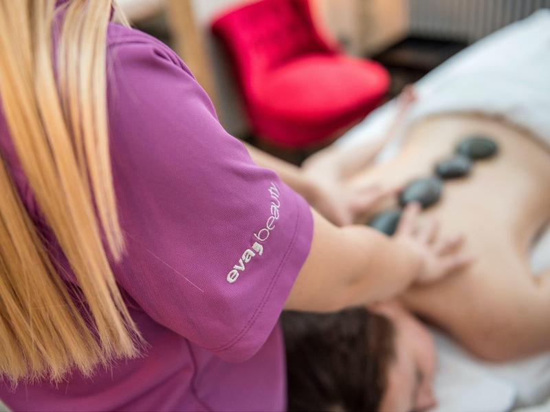 Therapeutin legt heiße Steine auf den Rücken einer Person zur Massage in hellem Raum.