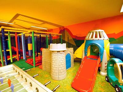 Buntes Indoor-Spielzimmer mit Klettergerüst, Rutsche, Fußballtisch und Spielzeugauto.