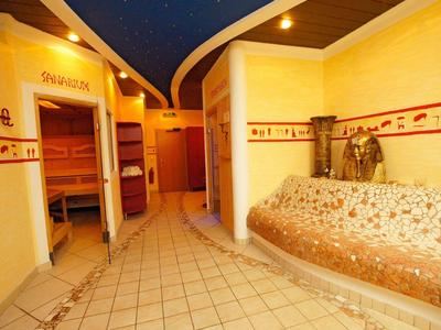 Innenraum eines Wellnessbereichs mit Saunazugang, Sitzbereich und warmem gelben Licht.