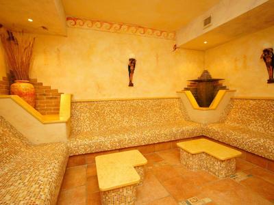 Ein gemütlicher Raum mit Mosaik-Sitzbänken, zwei kleinen Tischen und warmen gelb-orangenen Wänden.