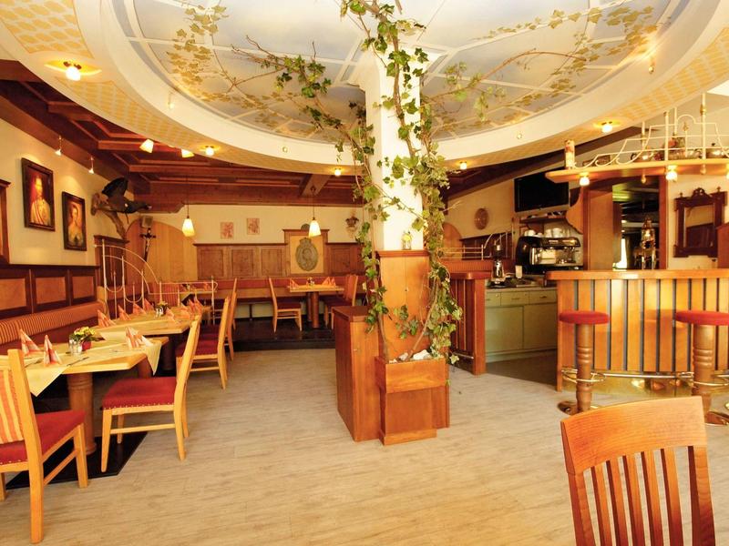 Gemütliches Restaurant mit Holzmöbeln, warmem Licht und einer Säule mit grünen Pflanzen in der Mitte.