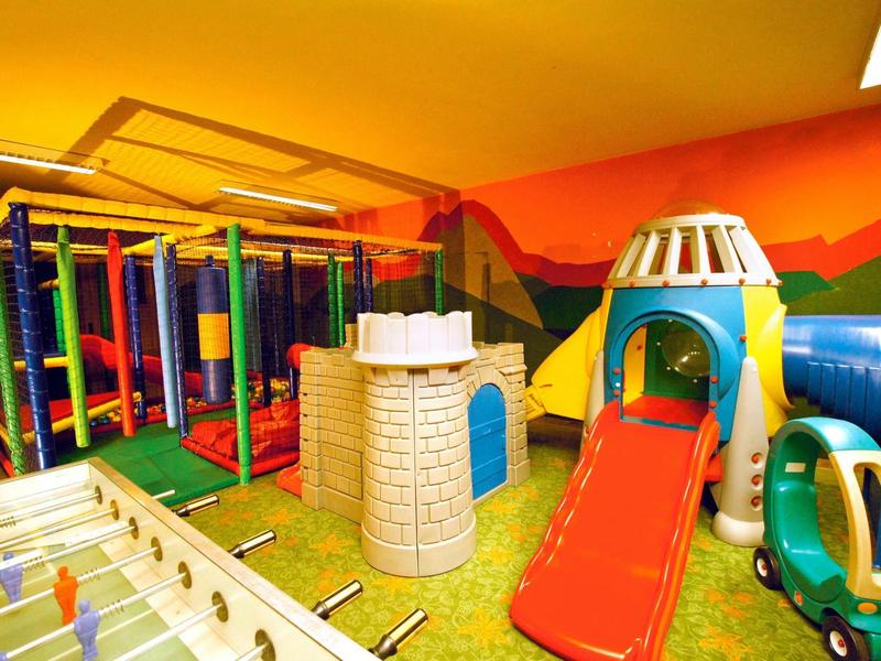 Buntes Indoor-Spielzimmer mit Klettergerüst, Rutsche, Fußballtisch und Spielzeugauto.