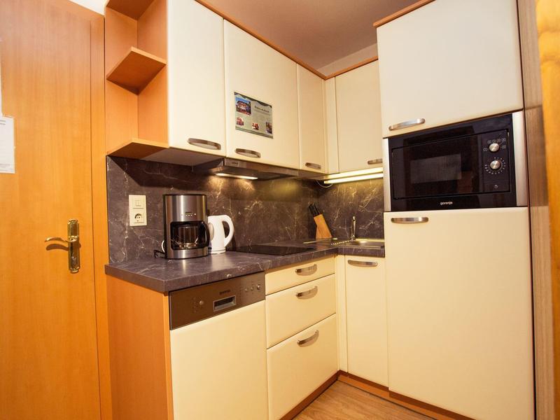 Kleine Küche mit cremefarbenen Schränken, grauer Arbeitsplatte und eingebauten Geräten.