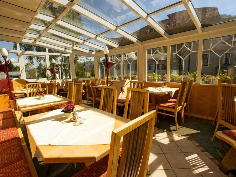 Helles, sonnendurchflutetes Restaurant mit Holzmöbeln und Glasdach, dekoriert mit Blumen.