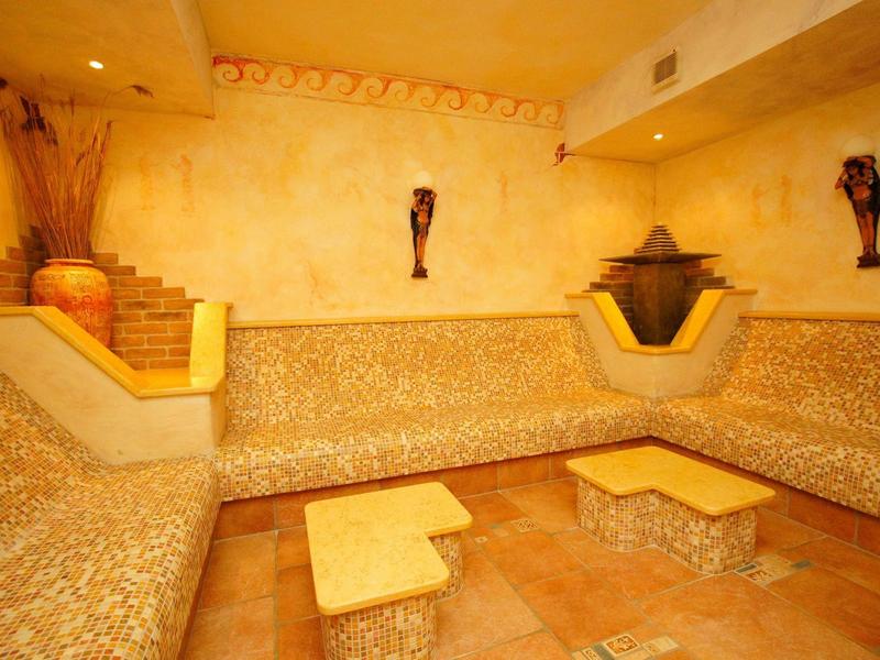 Ein gemütlicher Raum mit Mosaik-Sitzbänken, zwei kleinen Tischen und warmen gelb-orangenen Wänden.