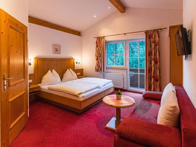 Habitación de hotel acogedora con cama doble, alfombra roja, zona de estar y balcón.