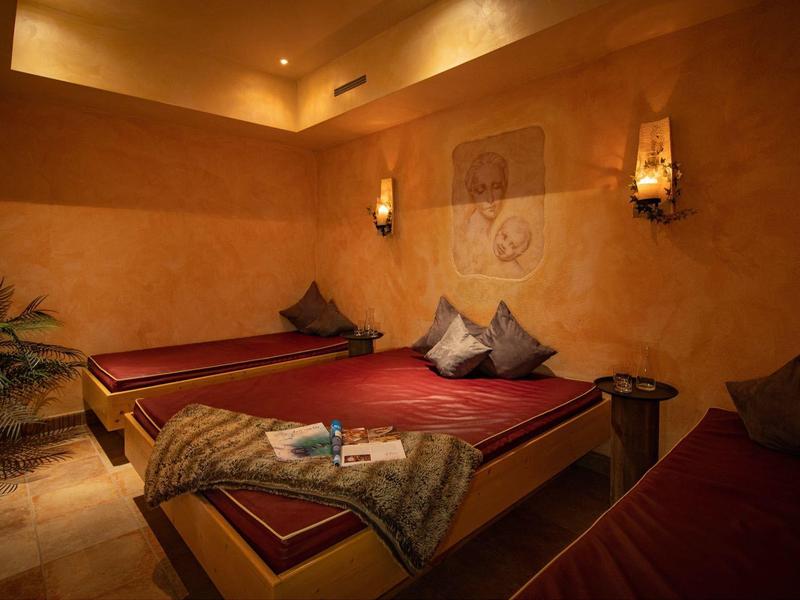 Ein gemütlicher Raum mit drei roten Liegen, weichen Kissen und warmer Beleuchtung.