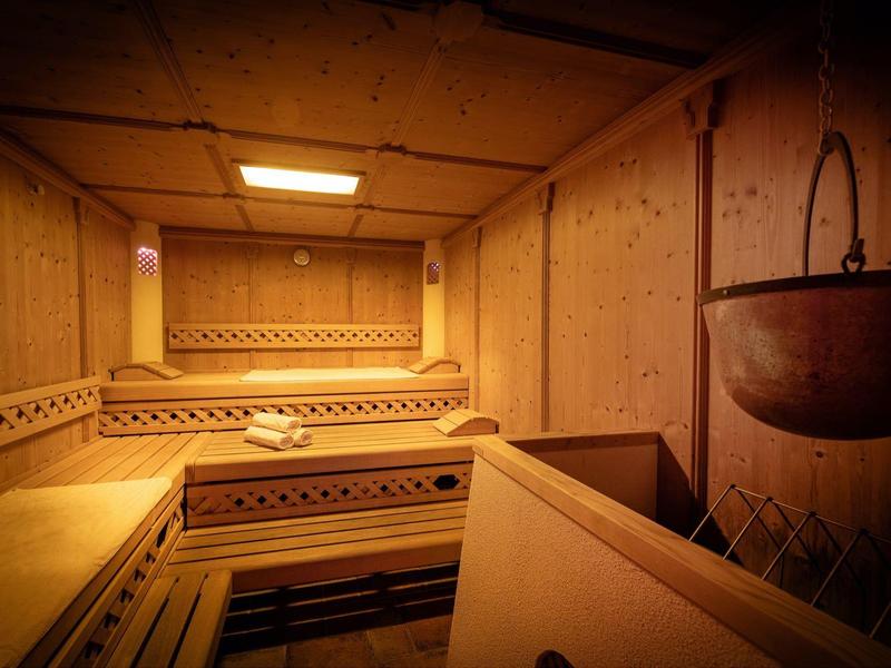 Holzsauna mit beleuchteten Bänken und hängendem Kupferkessel an der Wand.