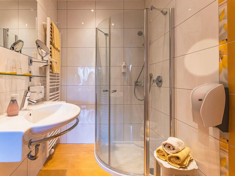 Helles Badezimmer mit runder Duschtür, weißem Waschbecken und hellbraunem Fliesenboden.