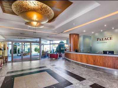 Ruime hotel lobby met receptie, zithoeken en moderne verlichting.