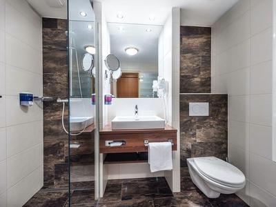 Modernes Badezimmer mit braunem Waschbecken, weißer Toilette und Glastür zur Dusche.