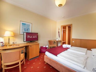 Gemütliches Hotelzimmer mit Doppelbett, Schreibtisch, Fernseher und warmem Licht, rote Teppichfarbe.