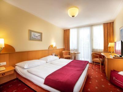Hell eingerichtetes Hotelzimmer mit Doppelbett, roten Akzenten und Balkonfenster.