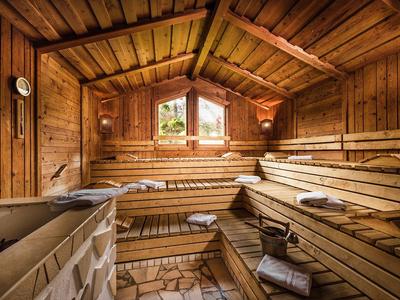 Holzsauna mit gestuften Bänken, Fenster, Eimer, Kelle und Handtüchern auf Holzboden.