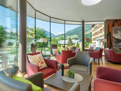 Accogliente zona lounge dell'hotel con grandi finestre panoramiche che si affacciano su montagne e villaggio.