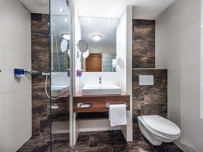 Modernes Badezimmer mit braunem Waschbecken, weißer Toilette und Glastür zur Dusche.