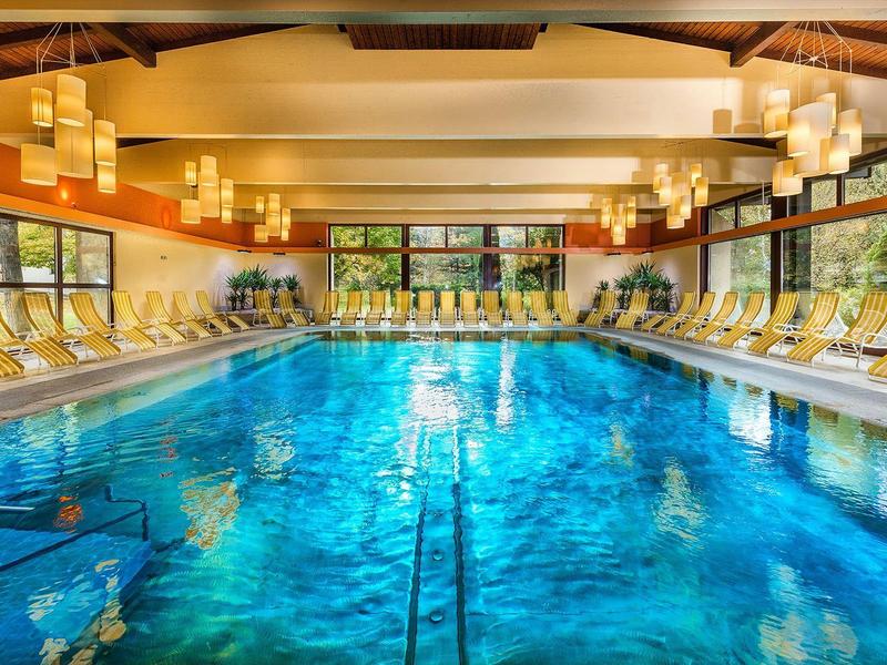 Großes Hallenbad mit klar blauem Wasser, beigen Liegestühlen und warmem Licht.