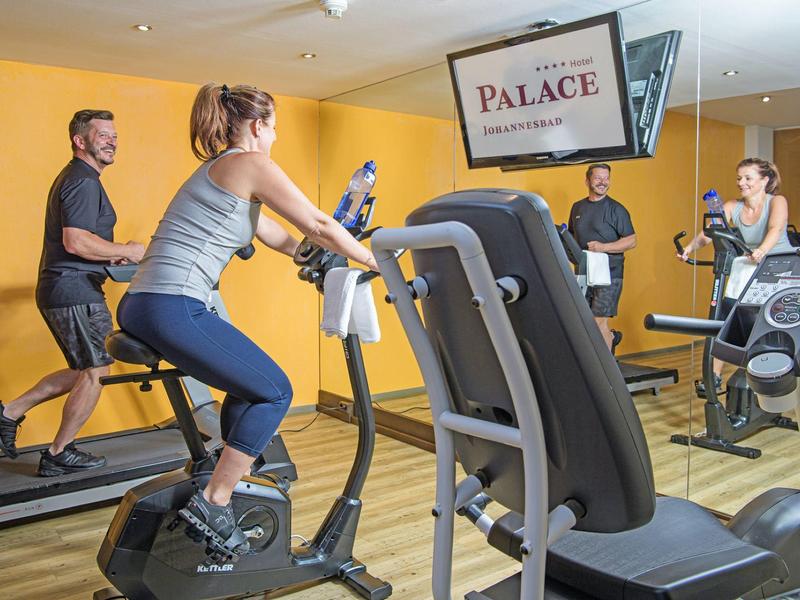 Vier Personen trainieren auf Fahrradergometern in einem hellen Fitnessraum mit Holzboden.