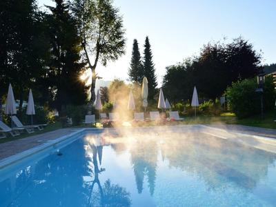 Schwimmbecken morgens mit Nebel, umgeben von weißen Sonnenschirmen und Bäumen im Hintergrund.