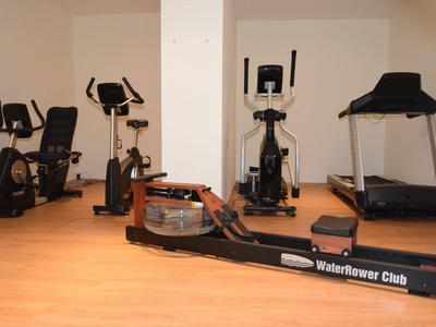 Salle de sport avec différents équipements comme vélo, elliptique et tapis roulant.